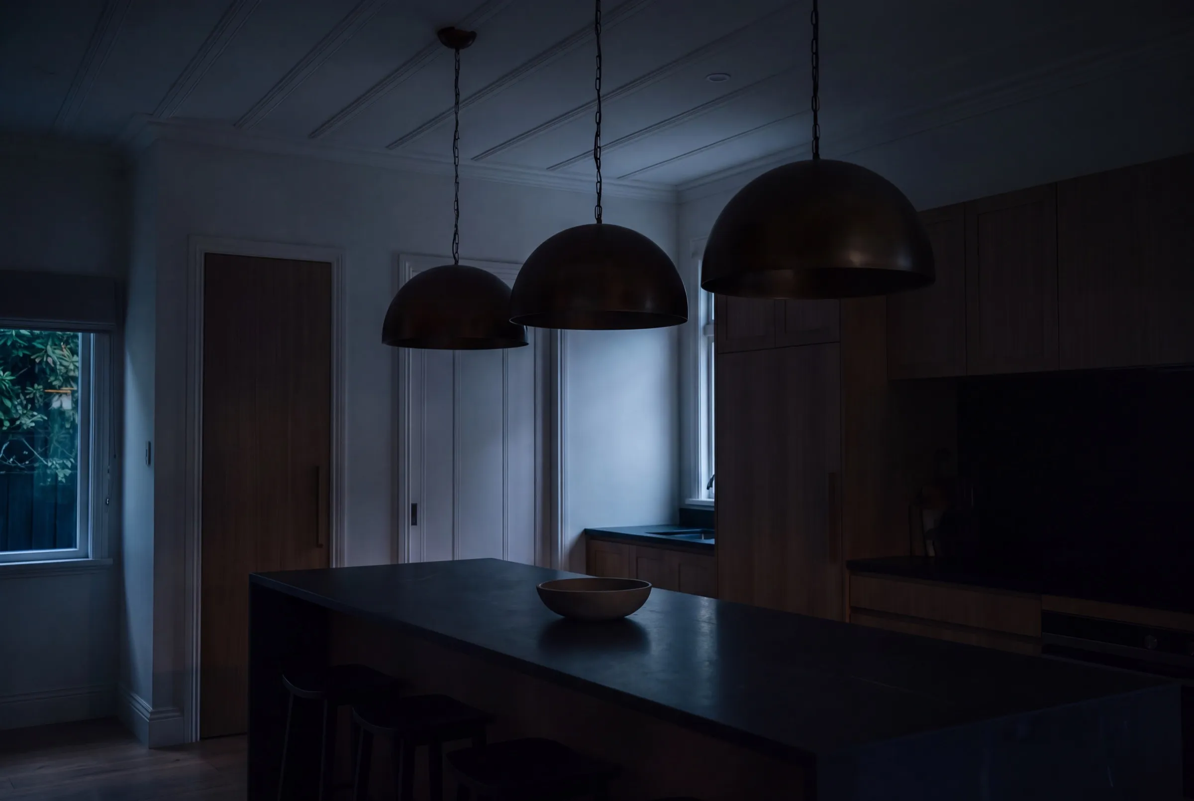 Kitchen island under three bronze dome pendants at dusk